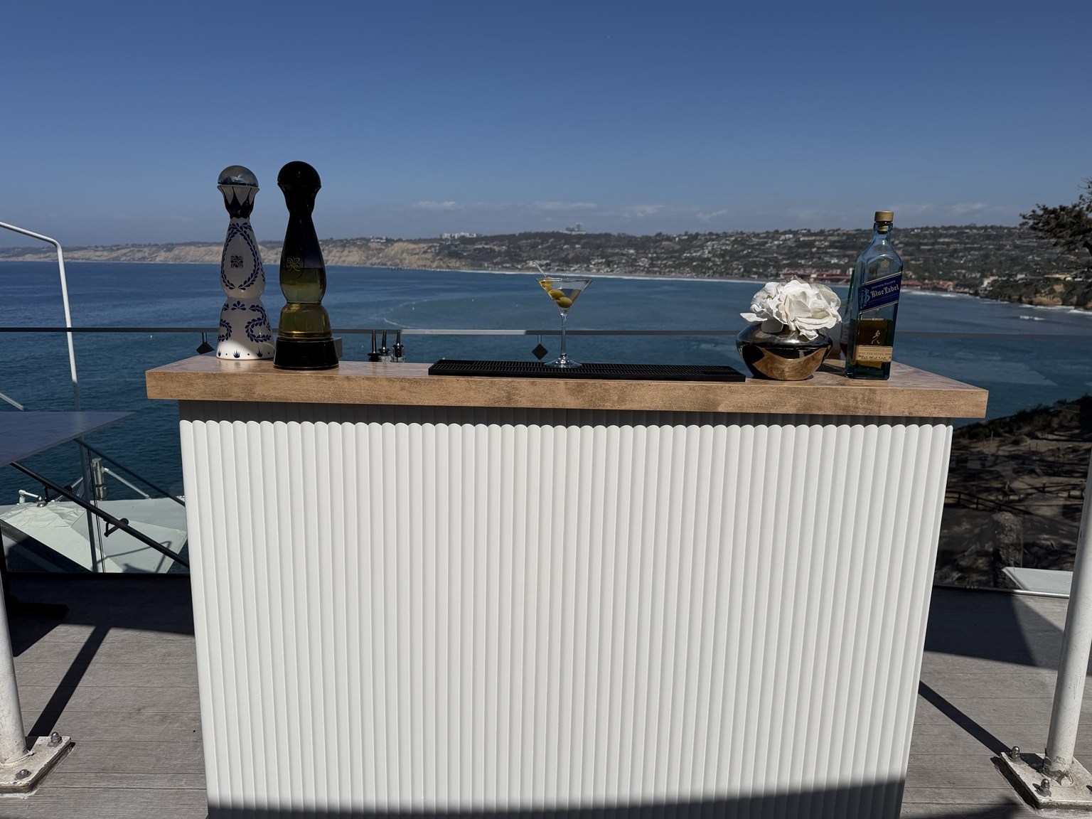 NEED Hospitality's white fluted mobile bar with warm wood countertops set against the San Diego ocean